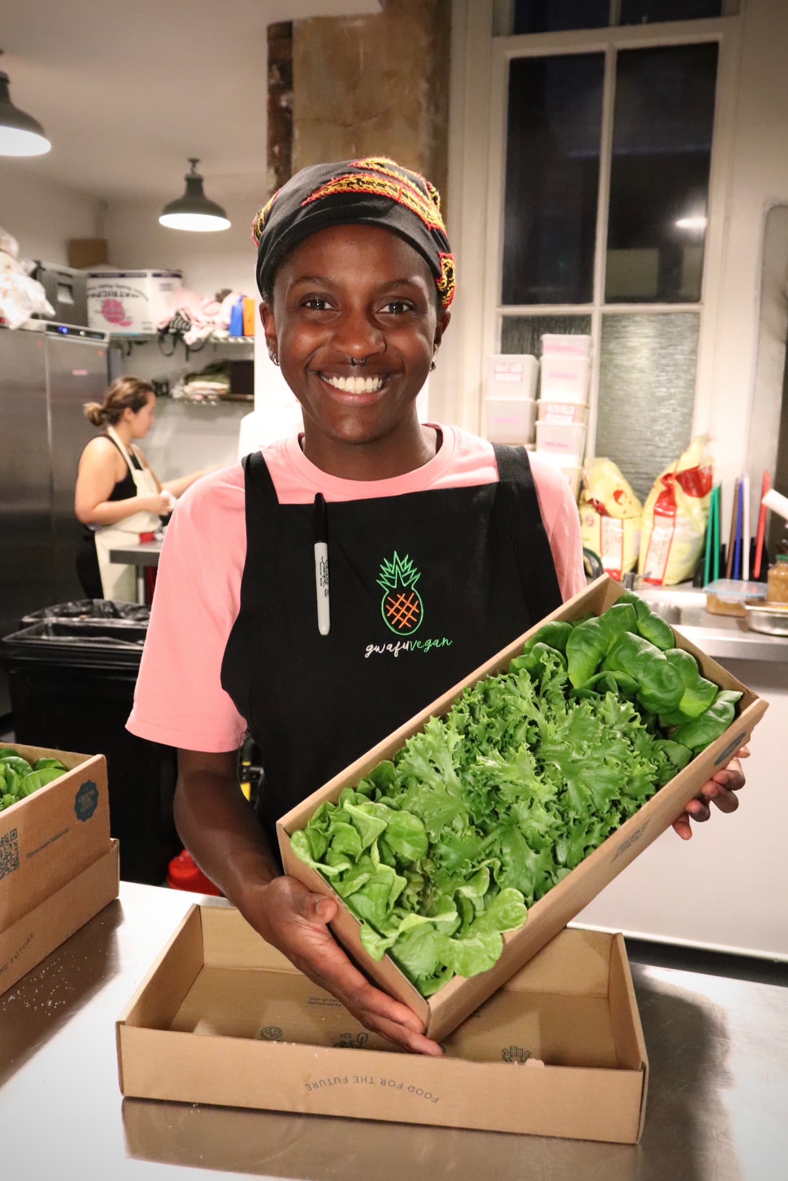 A cook smiling while holding a tray of fresh lettuces